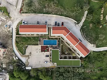 Letecký pohled na moderní bytový komplex s červenou střechou a venkovním bazénem, obklopený zelení, parkovištěm a svěžími zahradami.