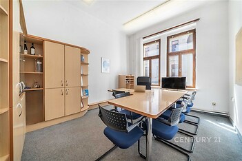 Kancelářský prostor s moderním nábytkem, velkými okny a kobercovou podlahou poskytuje světlé a příjemné pracovní prostředí.