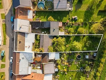 Pohled na rozlehlou zahradu s trávníkem a ovocnými stromy za rodinným domem, kde je situován dům s plechovou střechou a příjezdovou cestou.