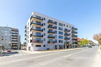 Moderní bytový dům s velkými okny a balkony, exteriér v minimalistickém stylu, nacházející se na klidné ulici.