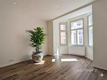 Světlý obývací pokoj s velkými okny, parketovou podlahou a moderním designem, ideální pro příjemné bydlení v centru města.