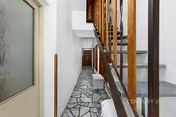 Chodba s kameninovou dlažbou, dřevěným zábradlím a vstupními dveřmi. Funkční design a přírodní materiály přinášejí moderní pocit.