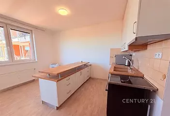 Kuchyňský kout s moderními skříňkami, světlou dřevěnou podlahou a velkými okny, které poskytují dostatek přirozeného světla