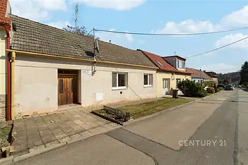 Fasáda rodinného domu s dlážděným dvorkem, šikmou střechou a dřevěnými dveřmi, vhodný k rekonstrukci v klidné lokalitě.