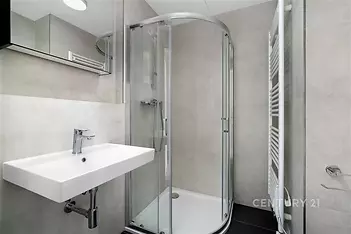 Moderní koupelna s proskleným sprchovým koutem, elegantní dlažbou a praktickým topným žebříkem vytváří stylový a funkční prostor.