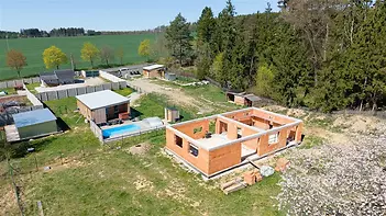 Stavební pozemek se zahájenou konstrukcí domu, obklopený zelení, cihlová stavba, klidná lokalita, možnost dokončení výstavby podle vlastních představ