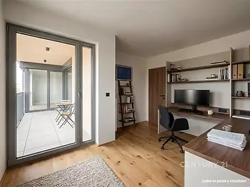 Domácí kancelář s parketovou podlahou, moderním nábytkem a velkými okny vedoucími na prostorný balkon nabízí světlé a klidné pracovní místo.