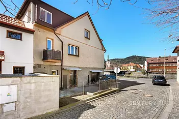 Dvoupodlažní rodinný dům s malým balkonem nabízí výhled na klidnou dlážděnou ulici s parkovacími možnostmi, zachovalá fasáda a klidné okolí.