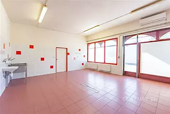 Světlá víceúčelová místnost s dlažbou, velkými okny a moderním osvětlením, ideální pro komerční využití nebo rekonstrukci.