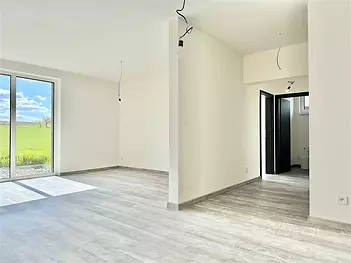 Světle obývací pokoj s velkými okny, moderní dřevěná podlaha a nově rekonstruovaný prostor, který nabízí otevřený výhled na krajinu.