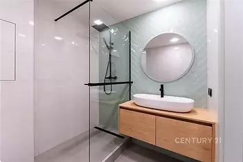 Moderní koupelna s proskleným sprchovým koutem, dřevěným umyvadlovým pultem a světlými obklady, které dodávají prostoru elegantní vzhled.