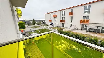 Balkon s moderním zábradlím, žluté sklo, výhled na udržovaný dvůr, novostavba bytového domu, klidná lokalita.