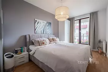 Prostorná ložnice s parketovou podlahou, velká okna poskytující dostatek světla, moderní interiér s elegantním osvětlením.