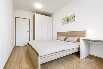 Prostorná ložnice s parketovou podlahou, vestavěné skříně a moderní nábytek, světlý interiér s minimalistickým designem.