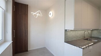 Moderní kuchyň s vestavěnými skříněmi, dlažbou a bílými skříňkami, vybavená elegantním osvětlením a nerezovým dřezem.