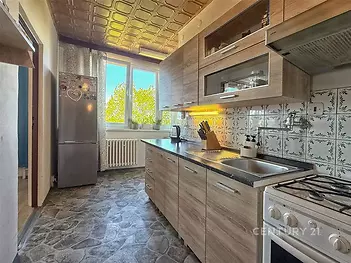 Kuchyň s moderními dřevěnými skříňkami, dlažba na podlaze a velkým oknem poskytujícím dostatek přirozeného světla, vhodná pro rodinné vaření.