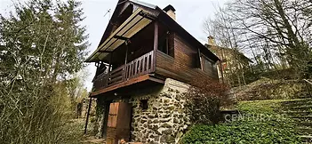 Dřevěná chata s kamennou podezdívkou, obklopená lesem, nabízí klidné prostředí. Rustikální design s balkónem a výhledem na přírodu.