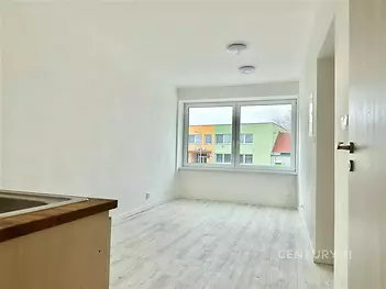 Světlý obývací pokoj s velkými okny, laminátovou podlahou a moderním designem, ideální pro útulné bydlení v rekonstruovaném bytě.