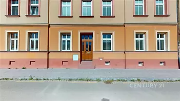 Historická fasáda bytového domu s dřevěnými dveřmi a velkými okny, udržovaná architektura a klidná lokalita poblíž centra.