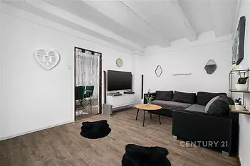 Světlý obývací pokoj s moderním nábytkem, parketovou podlahou a dekorativními prvky. Velká pohovka nabízí komfortní posezení.