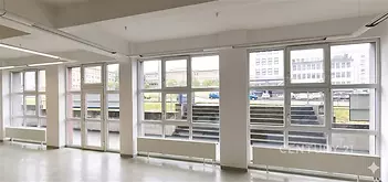 Světlá kancelářská místnost s velkými okny, moderní dlažbou a bílými stěnami, ideální pro kreativní pracovní prostředí.