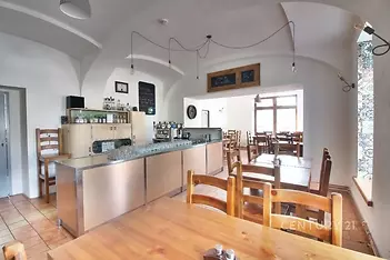 Prostorná jídelna s dlažbou a dřevěným nábytkem, velká okna poskytují dostatek světla, moderní barový pult z nerezové oceli.
