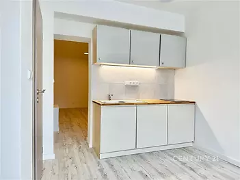 Kompaktní kuchyň se světlou dřevěnou podlahou, moderními skříňkami a světlými dlaždicemi nabízí praktický a stylový prostor v rekonstruovaném bytě.