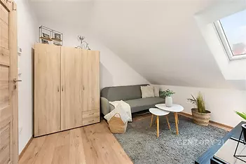 Podkrovní obývací pokoj s parketovou podlahou, střešními okny a moderním nábytkem, poskytující útulný a světlý prostor pro relaxaci.