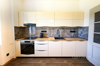 Moderní kuchyň s parketovou podlahou, vestavěnými skříněmi a elegantními spotřebiči, přináší stylové a funkční řešení pro domácnost.