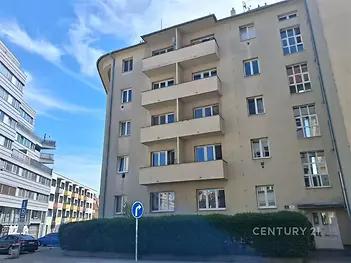 Fasáda bytového domu s moderním vzhledem, renovovaná okna a balkony, umístěná v klidné městské části s dostupností veřejné dopravy.
