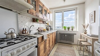 Světlá kuchyň s dřevěnými skříňkami, velkým oknem a dlažbou nabízí moderní atmosféru.