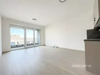 Světlý obývací pokoj s moderní parketovou podlahou, velká okna vedoucí na balkon, novostavba v minimalistickém stylu.