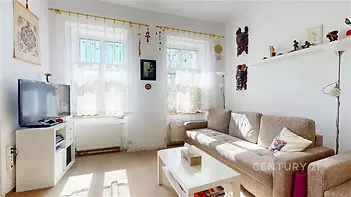 Světlý obývací pokoj s velkými okny, moderní dekorací a světlou sedačkou, parketová podlaha a bílý nábytek dodávají místnosti útulnost