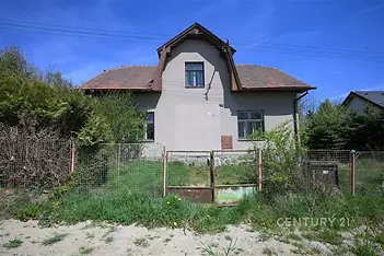 Rodinný dům s šedou fasádou a sedlovou střechou, přírodní zahrada, rekonstrukce nutná, klidná lokalita, ideální pro investici.