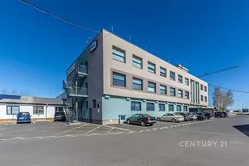 Moderní kancelářská budova s velkými okny, betonovou fasádou a parkovištěm, v dobrém stavu, ideální pro firemní prostory.