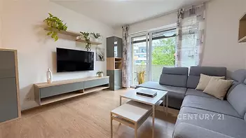 Světlý obývací pokoj s dřevěnou podlahou, velkými okny a moderním nábytkem.