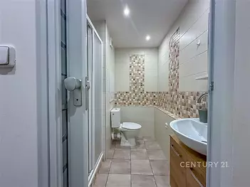 Moderní koupelna s dlažbou, sprchovým koutem a dřevěnou skříňkou pod umyvadlem, nabízí světlý interiér a kvalitní vybavení.