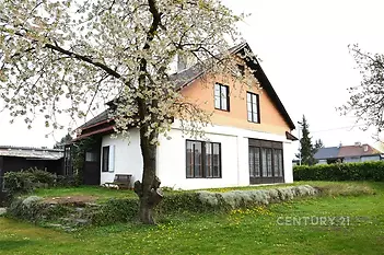 Rodinný dům s dřevěnou fasádou, velkými okny a prostornou zahradou. Nachází se v klidném prostředí, ideální pro rodinné bydlení.