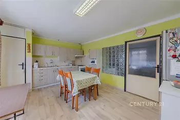 Světlá kuchyň s parketovou podlahou, moderními skříňkami a velkými okny. Vyniká prostorný jídelní stůl a svěží žlutozelené stěny.