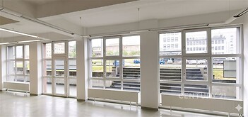 Světlá kancelářská místnost s velkými okny, moderní dlažbou a bílými stěnami, ideální pro kreativní pracovní prostředí.