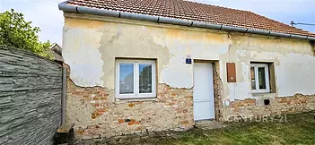 Exteriér staršího rodinného domu s fasádou v původním stavu, cihlovými detaily a šikmou střechou; ideální k rekonstrukci.