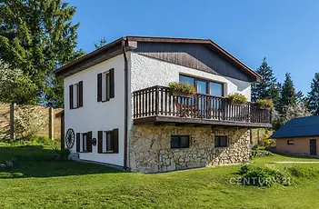 Dvoupatrový rodinný dům se zahradou, dřevěným balkonem a kamennou fasádou, situovaný v klidné přírodní lokalitě.