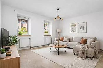 Světlý obývací pokoj s moderními betonovými podlahami, velkými okny a světlým nábytkem, vytvářejícími příjemnou atmosféru.