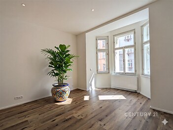 Světlý obývací pokoj s velkými okny, parketovou podlahou a moderním designem, ideální pro příjemné bydlení v centru města.