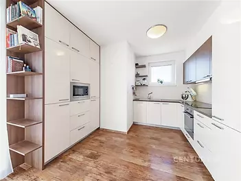 Moderní kuchyň s parketovou podlahou, světlými vestavěnými skříněmi a velkými okny.