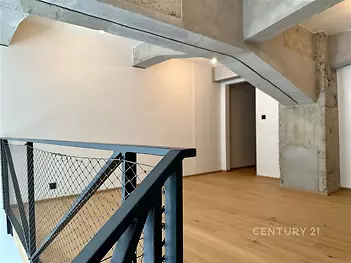 Moderní interiér s parketovou podlahou, odkryté betonové stropy a designové zábradlí; světlý a stylový prostor.