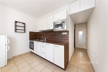 Kompaktní kuchyň s moderními bílými skříňkami, vestavěnou mikrovlnnou troubou a dlažbou. Světlý a prakticky zařízený prostor.