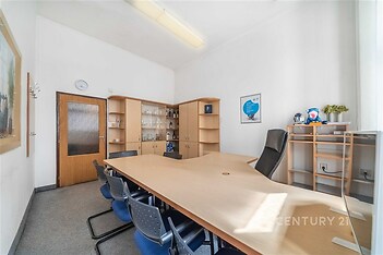 Kancelářská místnost s kobercem, prostorným dřevěným stolem a vestavěnými skříněmi. Velká okna zajišťují dostatek denního světla.