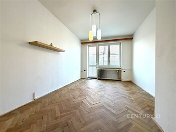 Světlý obývací pokoj s parketovou podlahou, velká okna, moderní lustr, prostor pro vestavěné skříně, příjemná atmosféra.