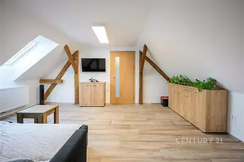 Podkrovní obývací pokoj s dřevěnou podlahou, masivním nábytkem a šikmým stropem poskytuje útulnou atmosféru a moderní styl bydlení.